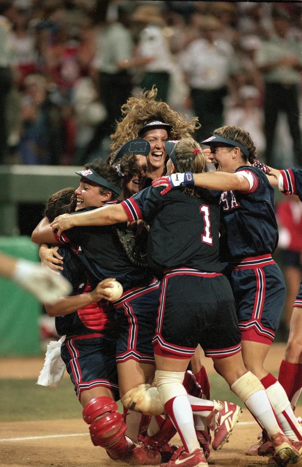 Softball players from Team USA joyfully celebrate on the field, hugging each other after a game