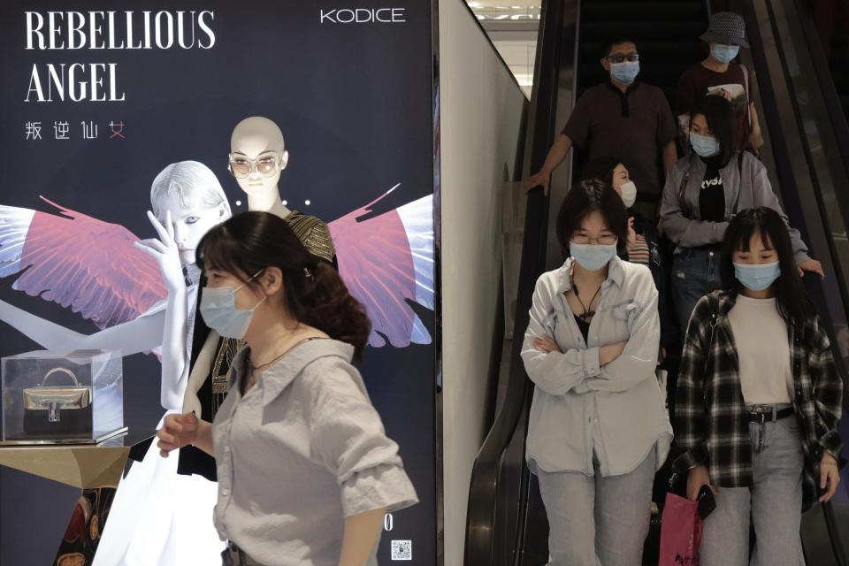 People wearing protective face masks ride an escalator.