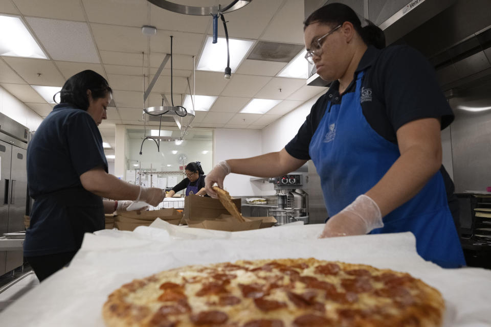 Cafeteria workers prepare pizza for student lunches at Firebaugh High School in Lynwood, Calif. on Wednesday, April 3, 2024. Demand for school lunches has increased after California guaranteed free meals to all students regardless of their family's income. Now, districts are preparing to compete with the fast food industry for employees after a new law took effect guaranteeing a $20 minimum wage for fast food workers. (AP Photo/Richard Vogel)