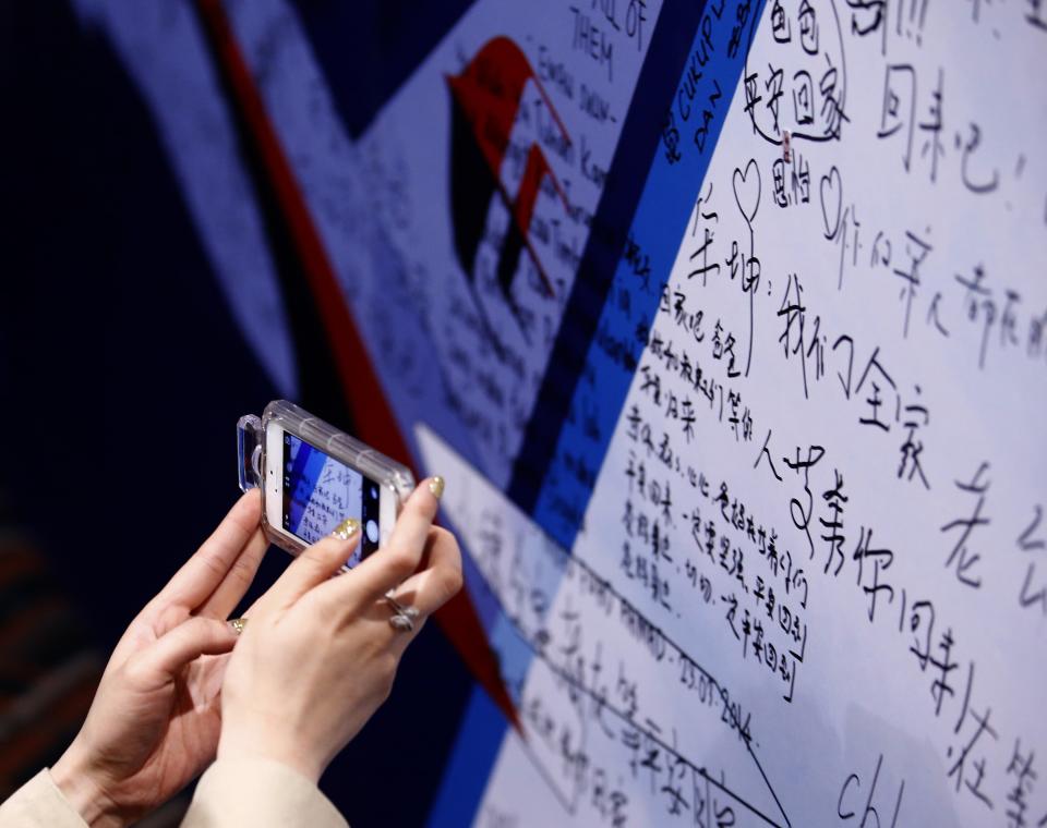A female journalist takes a picture of a message board with messages wishing the return of passengers aboard Malaysia Airlines MH370 at the Lido Hotel in Beijing