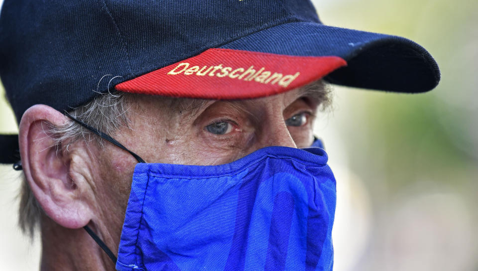 Due to the new coronavirus pandemic a man wears a face mask of the German first division soccer team FC Schalke 04 and a hat with the word reading "Deutschland" (Germany) in Gelsenkirchen, Germany, Wednesday, Aug. 12, 2020. (AP Photo/Martin Meissner)