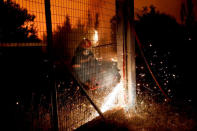 A firefighter cuts a metal fence as a wildfire burns near the village of Metochi, north of Athens, Greece, August 15, 2017. REUTERS/Giorgos Moutafis