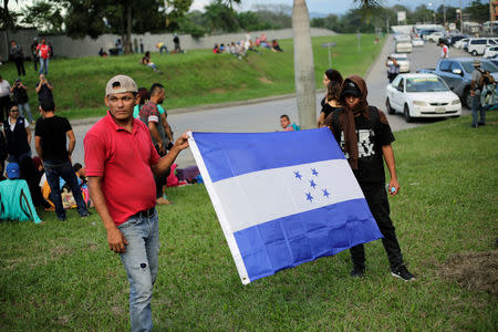 Hondurans hold a flag of Honduras as they wait to leave with a new caravan of migrants, set to head to the United States, at a bus station in San Pedro Sula, Honduras, January 14, 2019. REUTERS/Jorge Cabrera