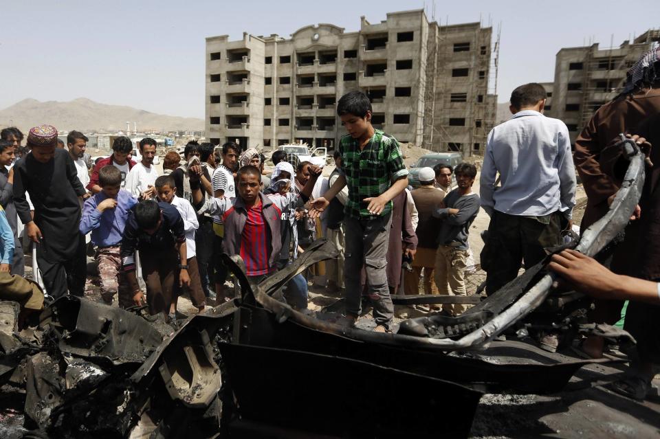 Afghans stand over the wreckage of a vehicle used in a car bomb attack at the north of Kabul International Airport in Kabul July 17, 2014. (REUTERS/Mohammad Ismail)