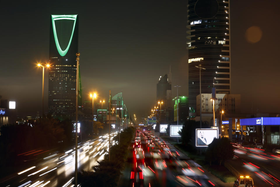 FILE - In this photo taken with a slow shutter speed, vehicles pass in front of the Kingdom Tower, left, in Riyadh, Saudi Arabia, Sept. 22, 2019. Saudi Arabia’s crown prince wants businesses, their employees and their families to move to the kingdom. The once ultraconservative capital, Riyadh, now promises a lifestyle where concerts, movie theaters, world class sporting events and deal-making are in abundance. Cultural heritage sites are also being revamped for tourists, distinguishing Saudi Arabia from other Gulf capitals defined by sprawling malls and high-rise hotels. (AP Photo/Amr Nabil, File)