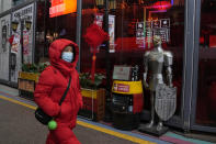 A woman wearing a mask to protect from the coronavirus walks past a coat of armour displayed outside a restaurant in Beijing, China, Friday, Jan. 21, 2022. The sweeping "zero-tolerance" policies that China has employed to protect its people and economy from COVID-19 may, paradoxically, make it harder for the country to exit the pandemic. (AP Photo/Ng Han Guan)