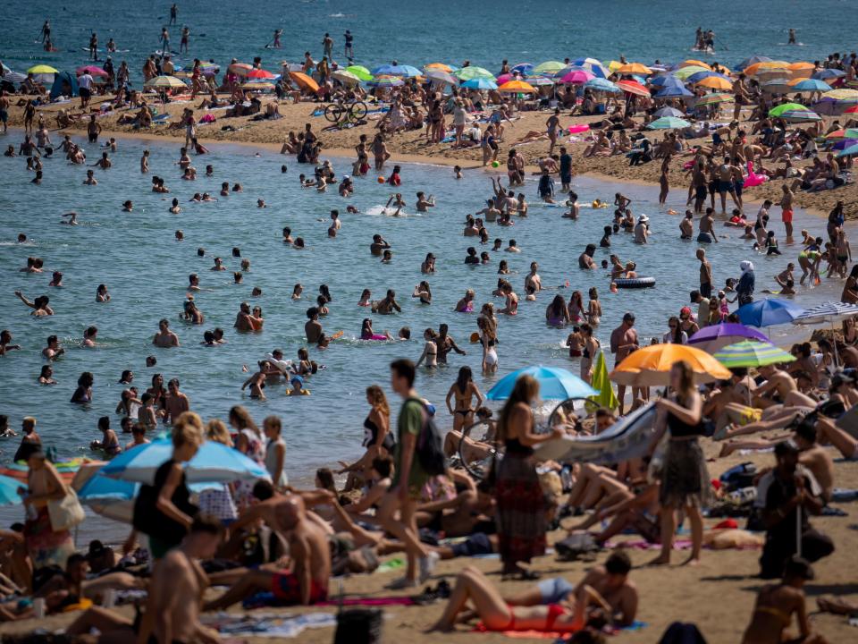 Scores of people sit at a beach in Spain.
