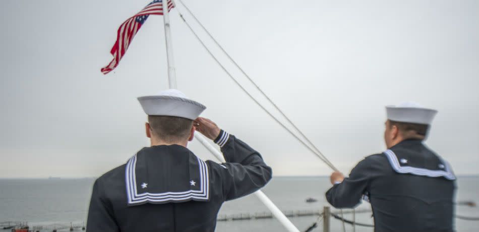 A sailor aboard the USS George HW Bush salutes the U.S. flag as another lowers it to half mast to honor the vessel's namesake after his death on December 1, 2018.