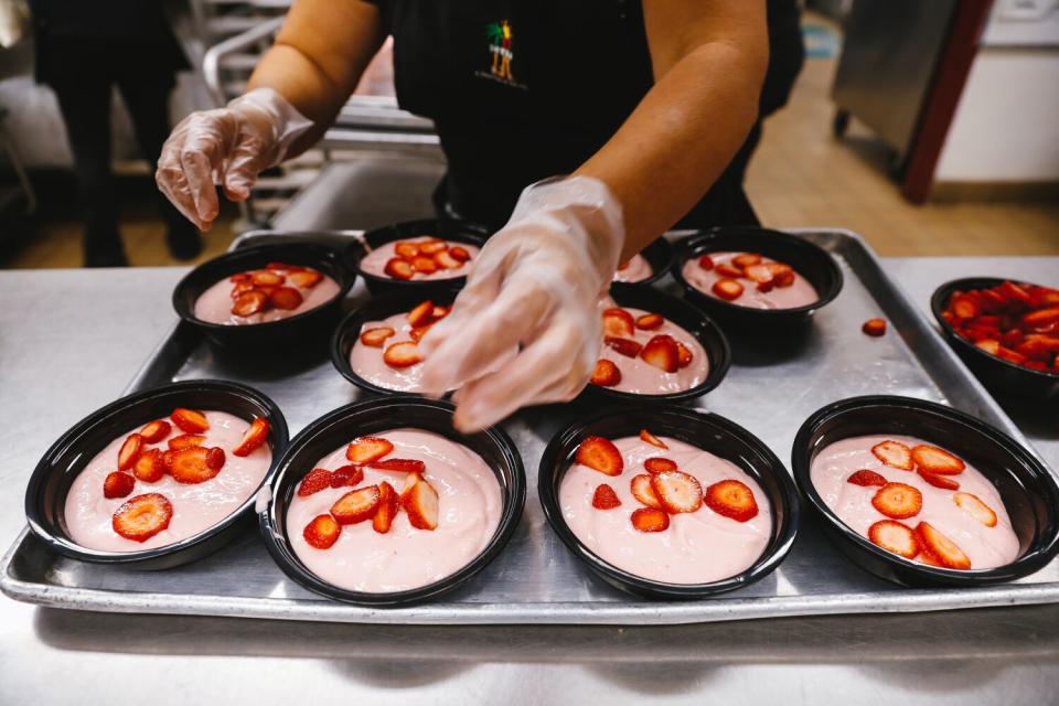 A cafeteria worker puts fresh strawberries on a tray of smoothie bowls.