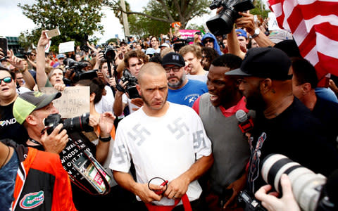 A man wearing a shirt with swastikas is forced away from the scene by the crowd moments after being punched by an unidentified member of the crowd near the site of a planned speech by white nationalist Richard Spencer, who popularized the term 'alt-right', at the University of Florida campus on October 19, 2017 in Gainesville - Credit: Getty