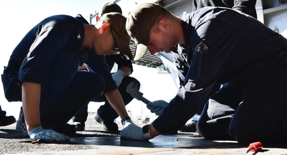 Machinist’s Mate 2nd Class Teran Vo, left, and Fireman Billy Price perform maintenance on a deck edge door track in the hangar bay aboard aircraft carrier USS Theodore Roosevelt, November 4, 2019.