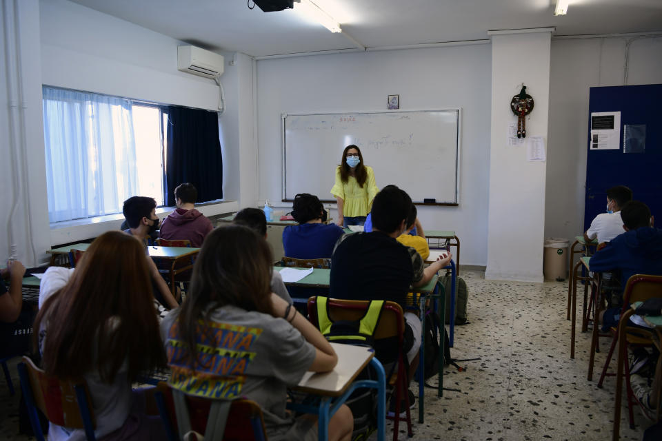 A teacher wearing a face mask to help curb the spread of the coronavirus, welcomes her students at a junior high school class in Athens, Monday, May 10, 2021. More than 1.1 million pupils and 127,300 teachers returned to school on Monday as primary and junior high school reopened its doors with mandatory home self-tests. (AP Photo/Michael Varaklas)