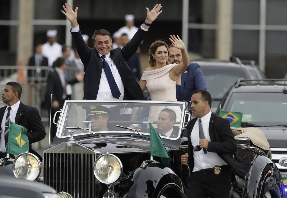 FILE - In this Jan. 1, 2019, file photo, flanked by first lady Michelle Bolsonaro, Brazil's President Jair Bolsonaro waves as he rides in an open car after his swearing-in ceremony in Brasilia, Brazil. The far-right leader’s first two weeks on the job have been filled with missteps and communication gaffes and little of his promised sweeping changes, underscoring a steep learning curve for a president elected on promises to overhaul much of daily life in Latin America's largest nation. (AP Photo/Andre Penner, File)