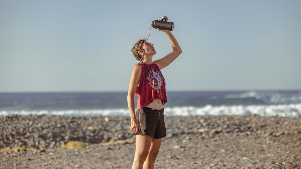 a runner on a beach pouring water over head