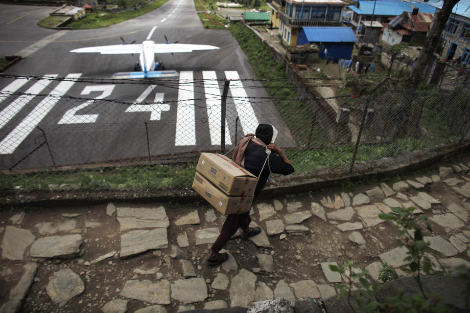 In this Friday, May 24, 2013 photo, a porter carries milk brought in by a flight, in Lukla, Nepal. Carved out of side of a mountain, the airport was built by Sir Edmund Hillary in 1965, and at an altitude of 2,843 meters (9,325 feet) it has earned the reputation of being one of the most extreme and dangerous airports in the world. (AP Photo/Niranjan Shrestha)