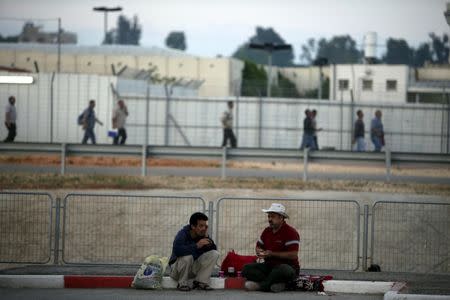 Palestinian labourers wait for work on the side of a road after crossing through Israel's Eyal checkpoint (seen in the background) from the West Bank town of Qalqilya, in this June 1, 2011 file photo. REUTERS/Nir Elias/Files