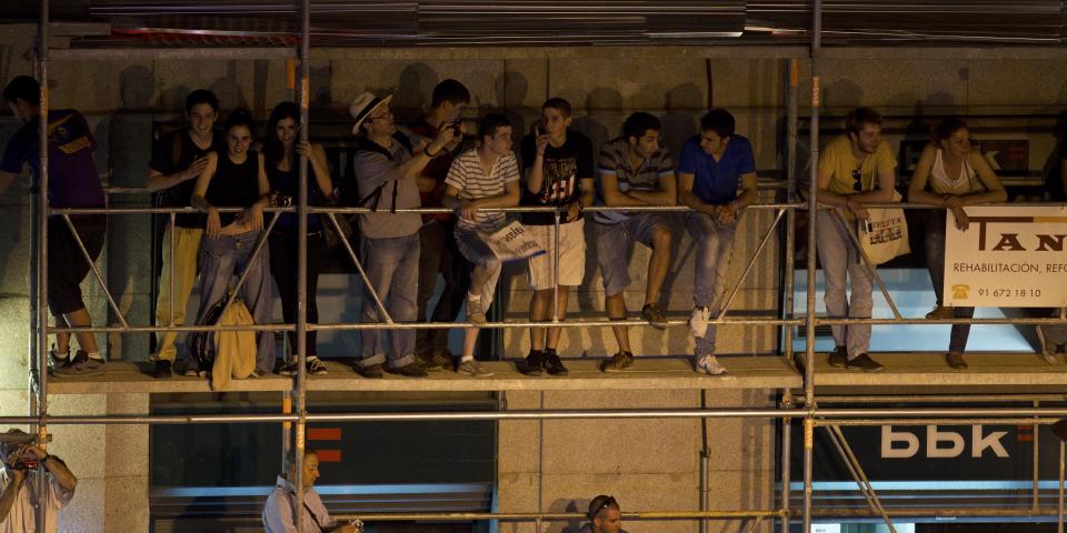 People look over the Puerta del Sol plaza after climbing some scaffolding in central Madrid Saturday May 12, 2012. The protesters returned to Sol to mark the anniversary of the protest movement that inspired groups in other countries. The protests began May 15 last year and drew hundreds and thousands of people calling themselves the indignant movement. The demonstrations spread across Spain and Europe as anti-austerity sentiment grew. (AP Photo/Paul White)