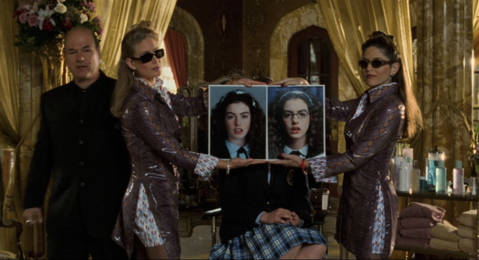 paolo's assistants holding up two unflattering pictures of mia before they reveal their make over