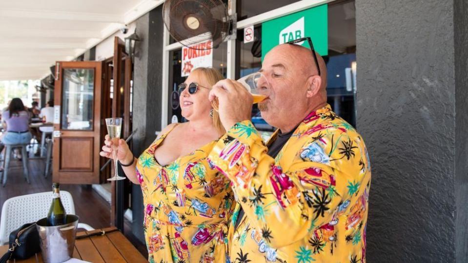 A man and a woman in brightly coloured clothes drink outside a pub