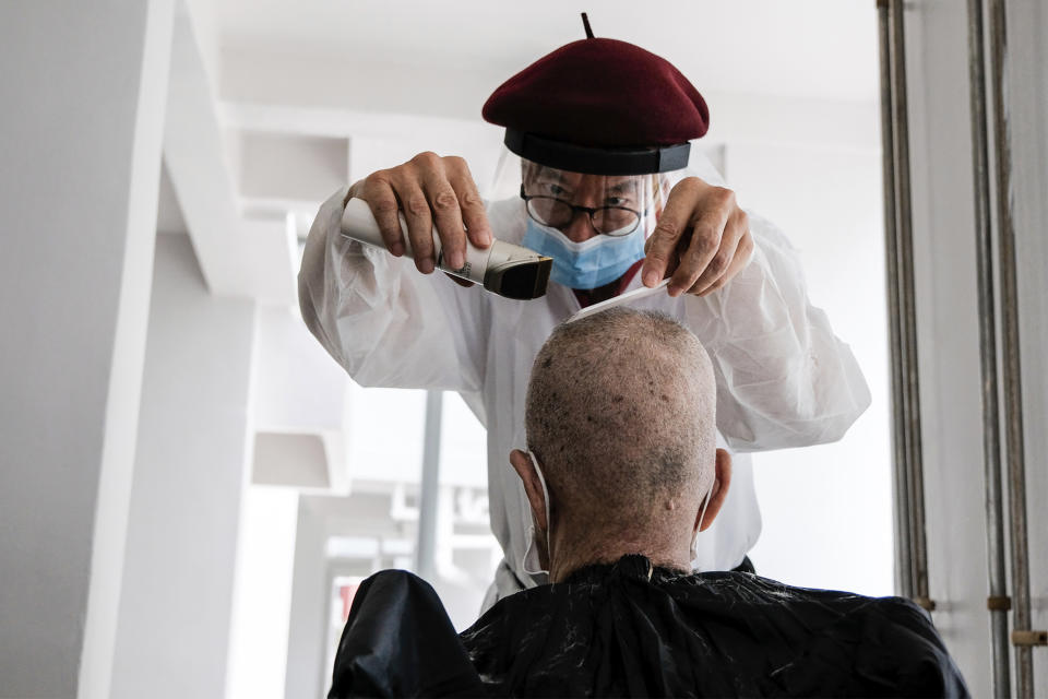 Keeping Hope Alive volunteer Mark Yuen, a trained hairdresser, provides a free haircut to an elderly man at the corridor of rental flat building Sunday, Oct. 4, 2020, in Singapore. Members of the volunteer group conduct weekend door-to-door visits to deliver goods or provide services to people in need. (AP Photo/Ee Ming Toh)