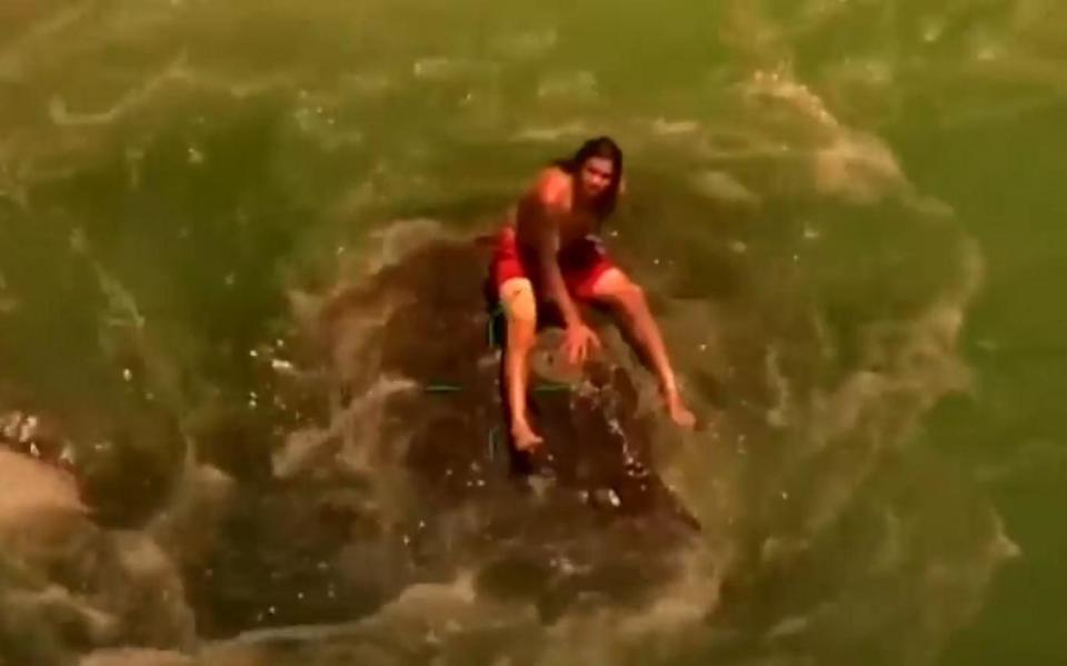 The swimmer clinging to the rocks before he is rescued