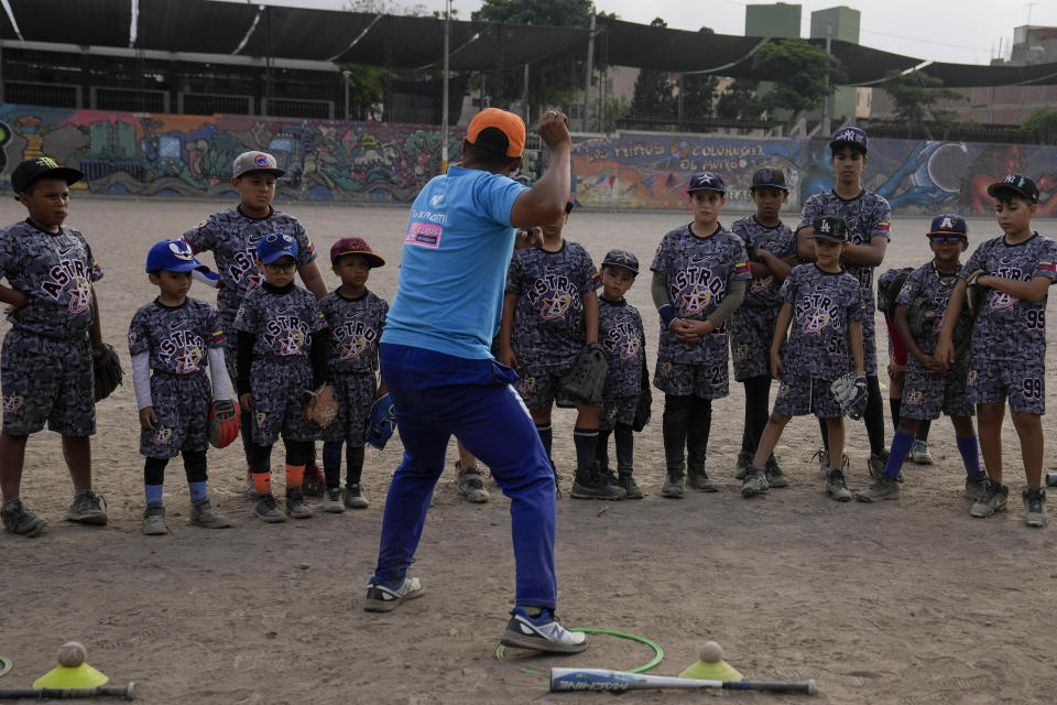 El entrenador de béisbol Franklin López enseña a varios niños migrantes venezolanos cómo lanzar la pelota durante un entrenamiento en un parque público de Comas, a las afueras de Lima, Perú, el 2 de mayo de 2024. (AP Foto/Martín Mejía)