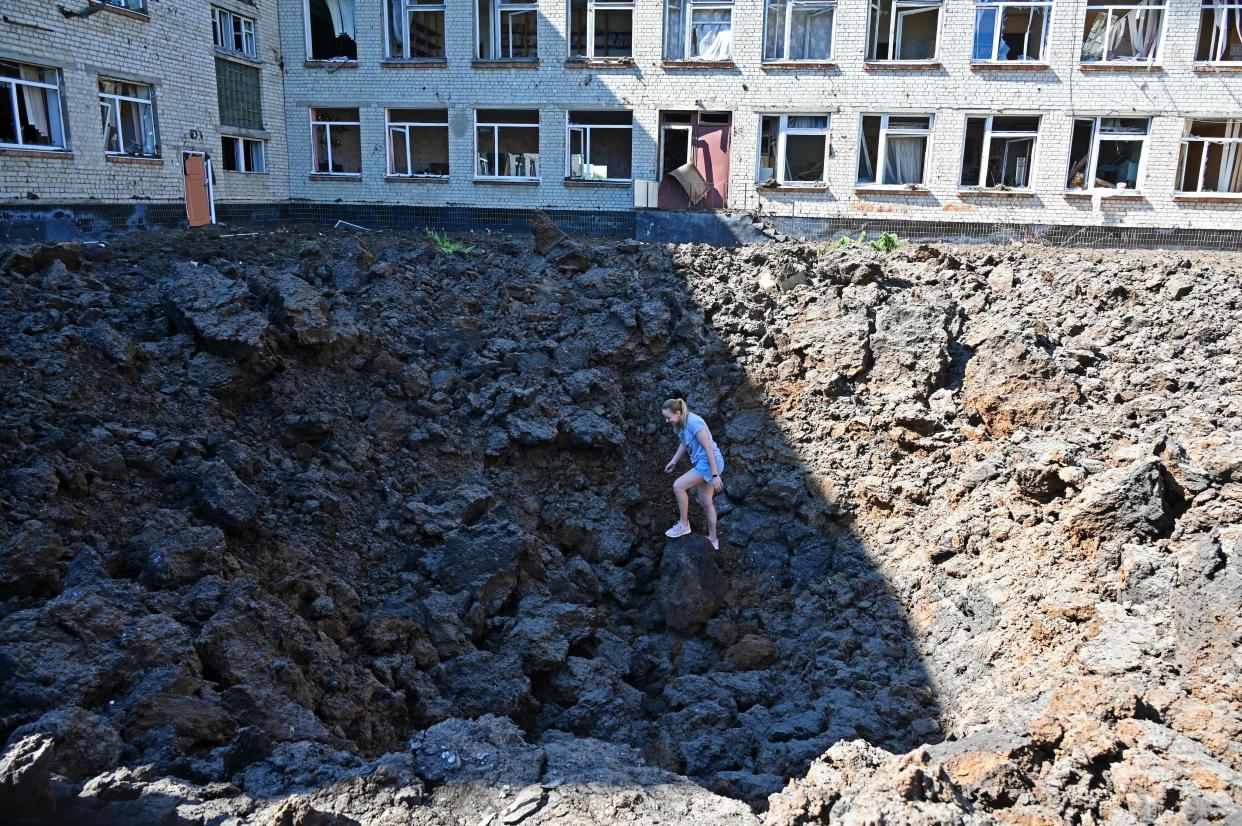 A woman stands in a crater caused by missile strikes which struck the yard of a school in a residential area of Kharkiv on June 27, 2022, amid the Russian invasion of Ukraine. 