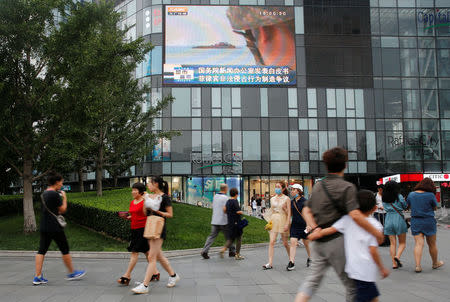 People walk past a screen showing a TV news broadcast about the South China Sea outside a shopping mall in Beijing, July 16, 2016. REUTERS/Thomas Peter