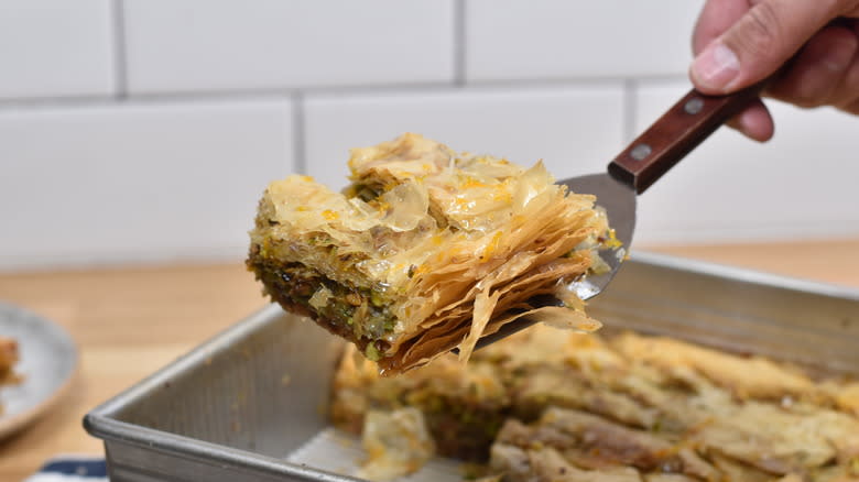 hand serving slice of baklava out of tray