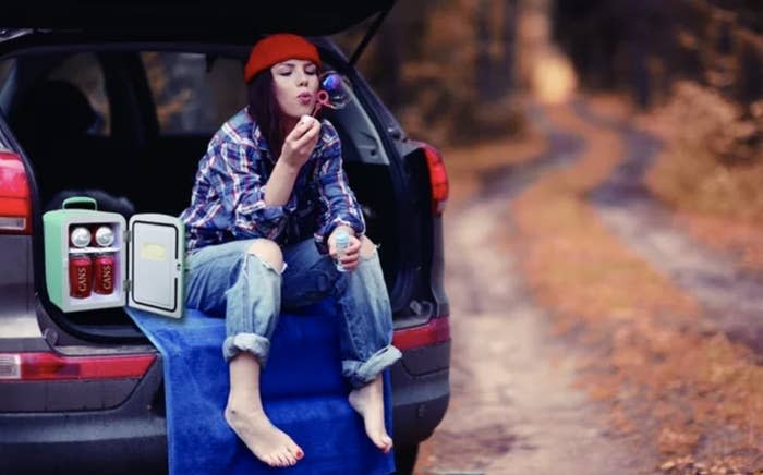 blue mini fridge next to model blowing bubbles and sitting in car trunk