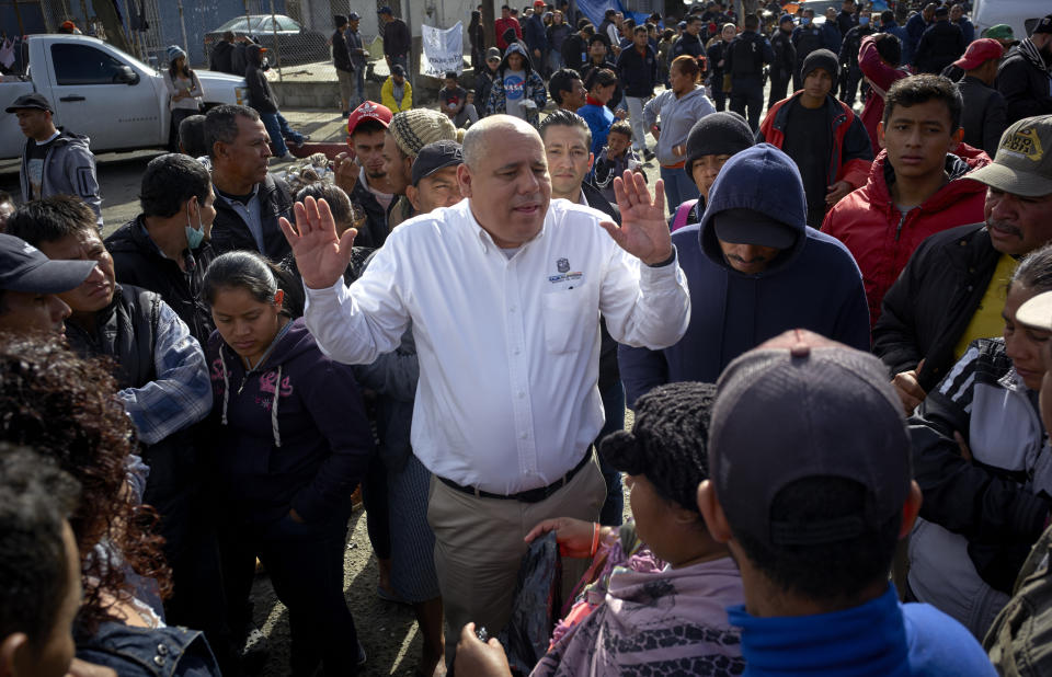 Luis Bustamante, an official from the Mexican state of Baja California, tries to answer questions from a group of Central American migrants, as they decide whether to relocate another shelter in Tijuana, Mexico, Friday, Nov. 30, 2018. Authorities in Tijuana said Friday they have begun moving Central American migrants from an overcrowded shelter on the border to an events hall further away. (AP Photo/Gregory Bull)