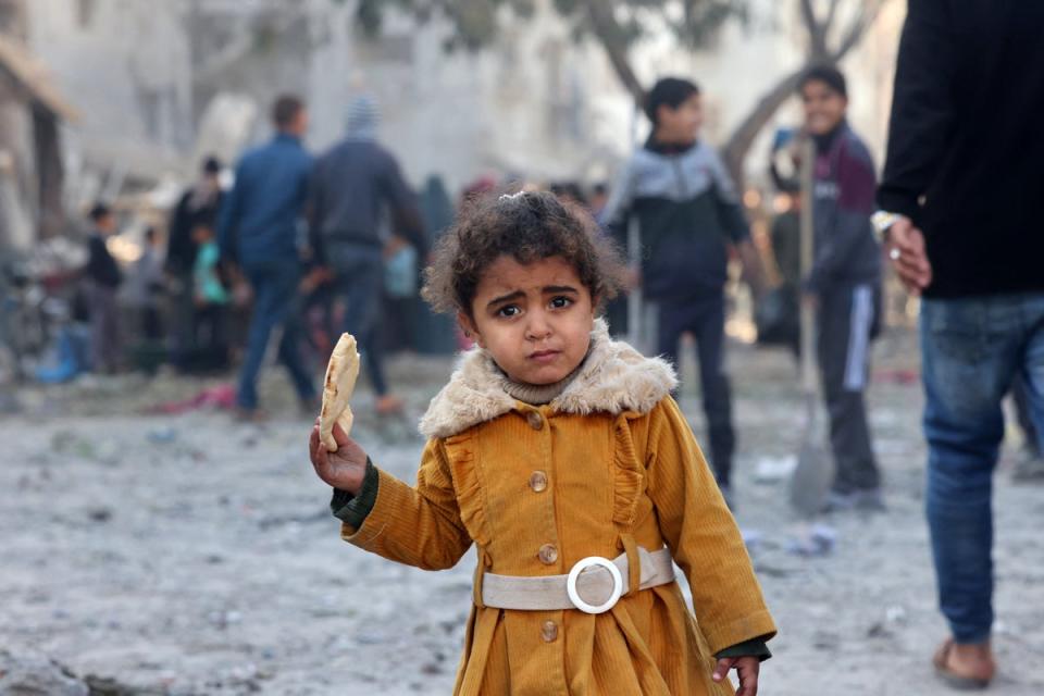 A Palestinian girl eats a piece of bread as people check debris on following overnight Israeli air strikes in Rafah refugee camp in the southern Gaza strip (AFP via Getty Images)