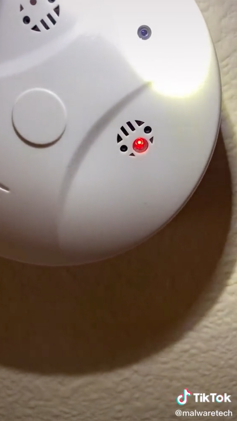 The same smoke alarm, when a flashlight is shined on it, now has a small blue light where the empty hole was