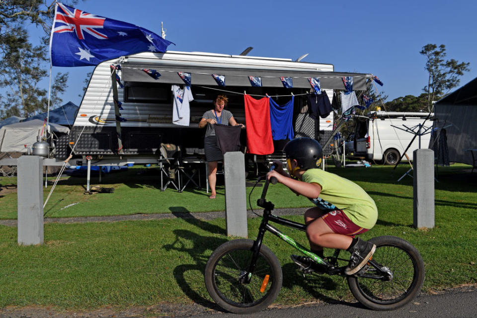 Holiday maker Debbie Coates in Lake Conjola, NSW, stands outside a caravan as a boy cycles past. 