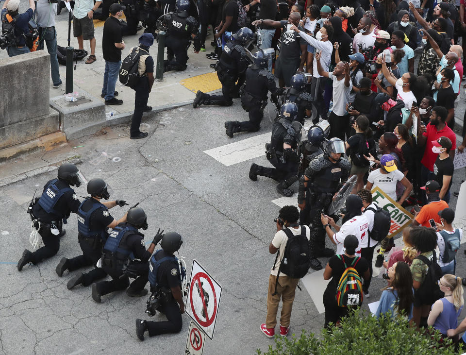 In a show of peace and solidarity, law enforcement officials with riot shields kneel in front of protesters Monday, June 1, 2020, during a fourth day of protests over the death of George Floyd in Minneapolis. (Curtis Compton/Atlanta Journal-Constitution via AP)