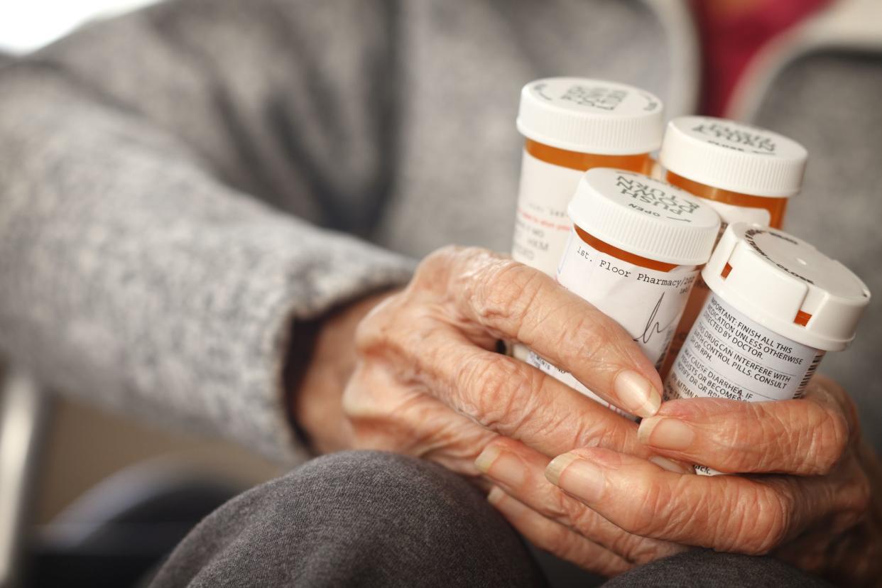 Senior citizen female holding bottles of prescription medicine sitting in a wheelchair.