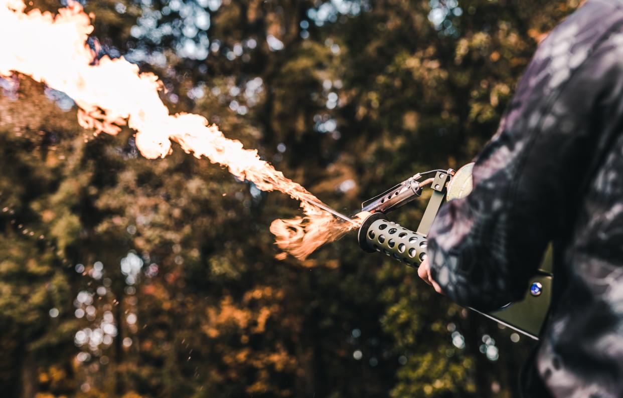 A person in a flannel shirt using a flamethrower in a forest