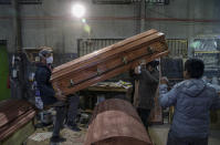 Coffin makers lift a casket at the Bergut Funeral Services factory in Santiago, Chile, Thursday, June 18, 2020. The coffin production has had to increase up to 120%, according to Nicolas Bergerie, owner of the factory. His more basic coffin model is called the COVID model and is made to cope with the increase of deaths during the coronavirus pandemic. (AP Photo/Esteban Felix)