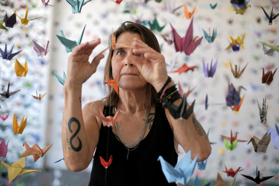 Artist Karla Funderburk, owner of Matter Studio Gallery, adjusts one of of the thousands of origami cranes hanging during an exhibit honoring the victims of COVID-19, Tuesday, Aug. 11, 2020, in Los Angeles. Funderburk started making the cranes three months earlier, stringing the paper swans in pink, blue, yellow and many other colors together and hanging them in her gallery. (AP Photo/Richard Vogel)