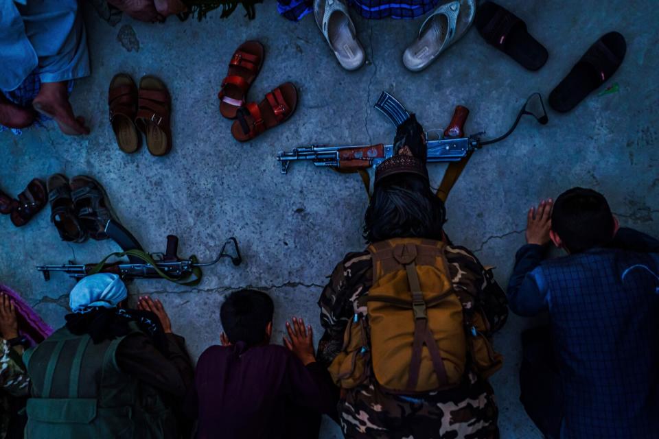 A top-down shot of men kneeling to pray with their sandals and rifles in front of them.