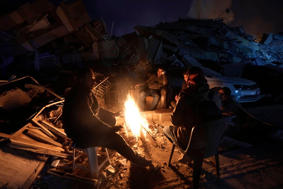 People warm up with fire in front of destroyed buildings in Antakya, southern Turkey (Copyright 2023 The Associated Press. All rights reserved.)