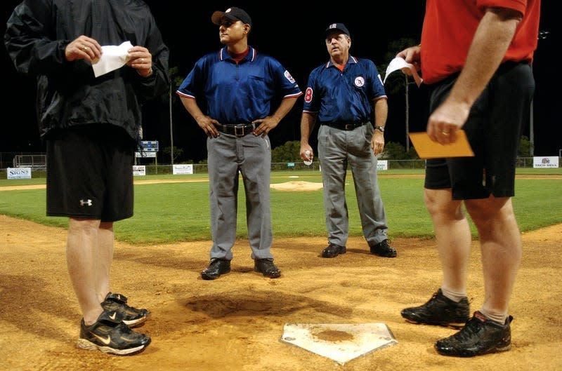 Little League umpire Joe Lemos, left, waits with fellow ump Dan Tipton, right, and Braden River manager Shawn Lewellen and San Marcos manager Craig Adams (foreground) before a recent game at the Englewood Sports Complex.