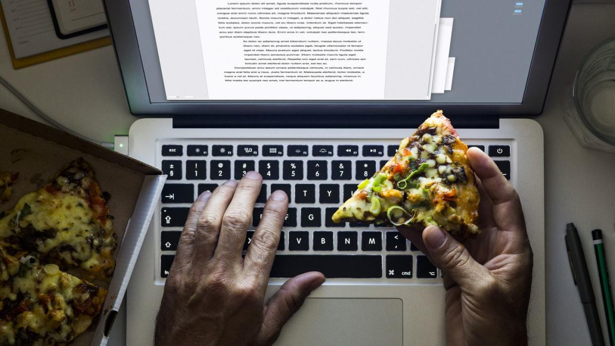 hand holding a pizza while working on a laptop