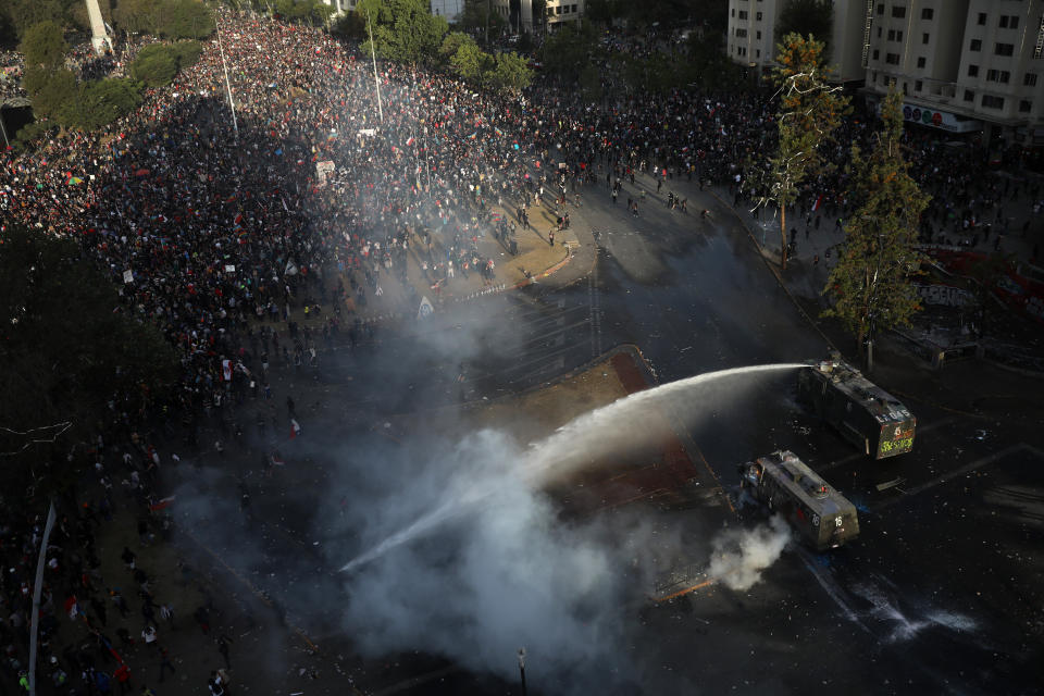 Demonstrators are sprayed by a police water cannon during an anti-government protest in Santiago, Chile, Friday, Nov. 1, 2019. Chile has been facing days of unrest, triggered by a relatively minor increase in subway fares. The protests have shaken a nation noted for economic stability over the past decades, which has seen steadily declining poverty despite persistent high rates of inequality. (AP Photo/Rodrigo Abd)