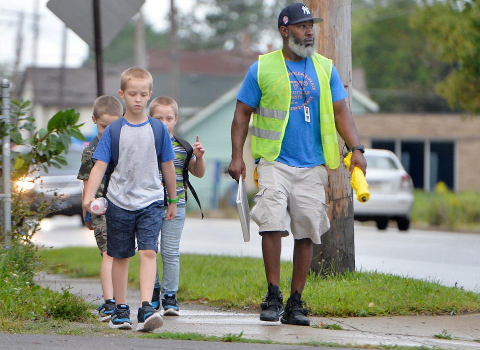 Craig Heidelberg, a member of the Blue Coats safety initiative, leads a walking school bus with Edison Elementary School students on the first day of school in Erie last fall.