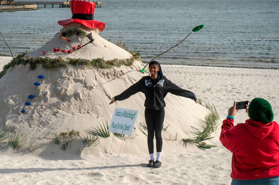 Visitors pose in front of Pass Christian’s “Sandyman”, which is a snowman made out of sand, on Pass Christian Beach on Thursday, Nov. 30, 2023.
