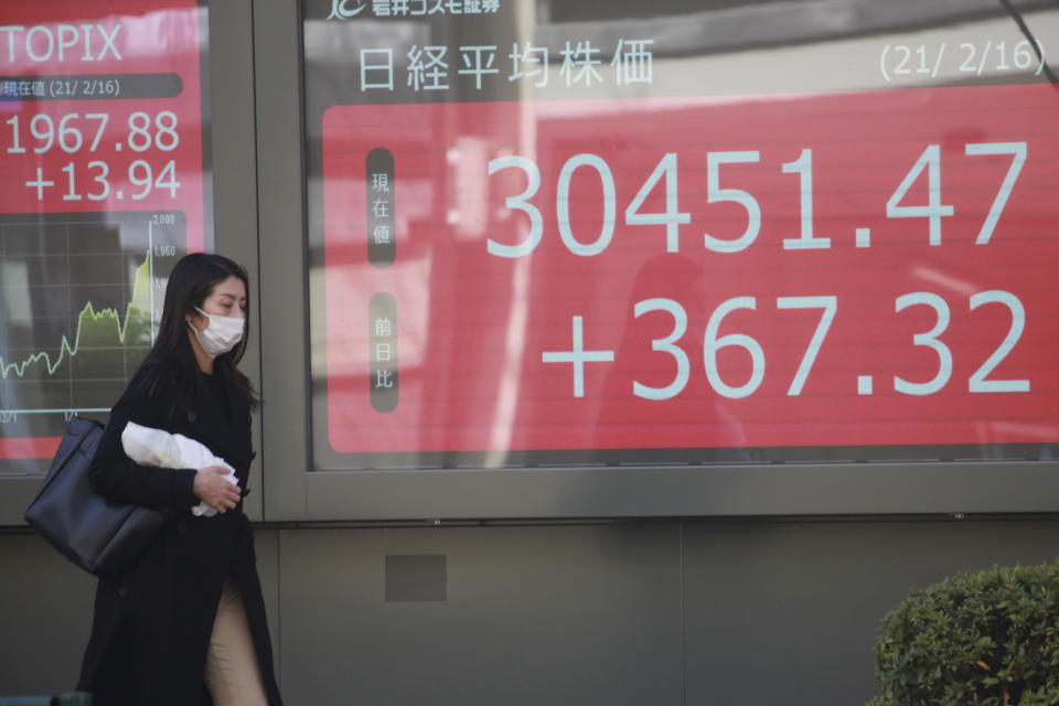 A woman wearing a face mask walks by an electronic stock board of a securities firm in Tokyo, Tuesday, Feb. 16, 2021. Asian shares advanced on Tuesday, lifted by the economic recovery, vaccine rollouts and signs that new coronavirus cases may be abating. (AP Photo/Koji Sasahara)