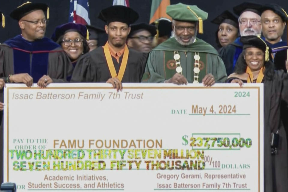 This image made from video provided by WCTV shows Gregory Gerami, a 30-year-old who called himself Texas' "youngest African American industrial hemp producer," third from left, and Florida A&M University president Larry Robinson pose with a ceremonial check while being surrounded by other university officials during a commencement ceremony on May 4, 2024 in Tallahassee, Fla. The $237 million donation was promised by Gerami, but everything was not what it seemed and the donation is now in limbo. Gerami maintains that everything will work out, but FAMU is not the only small university that has engaged with his major donation proposals only to see them go nowhere. (WCTV via AP)