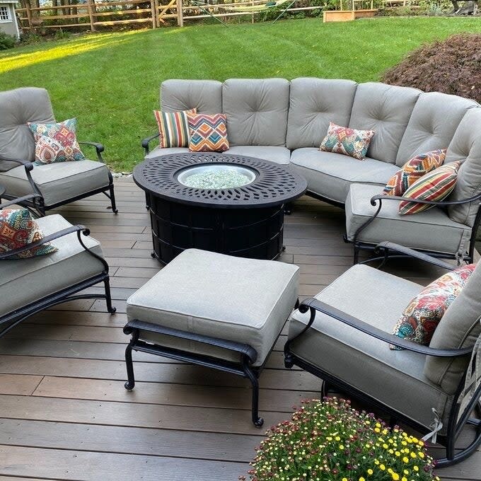 Patio furniture set with sofa, chairs, ottomans, and a fire pit table, arranged on a wooden deck