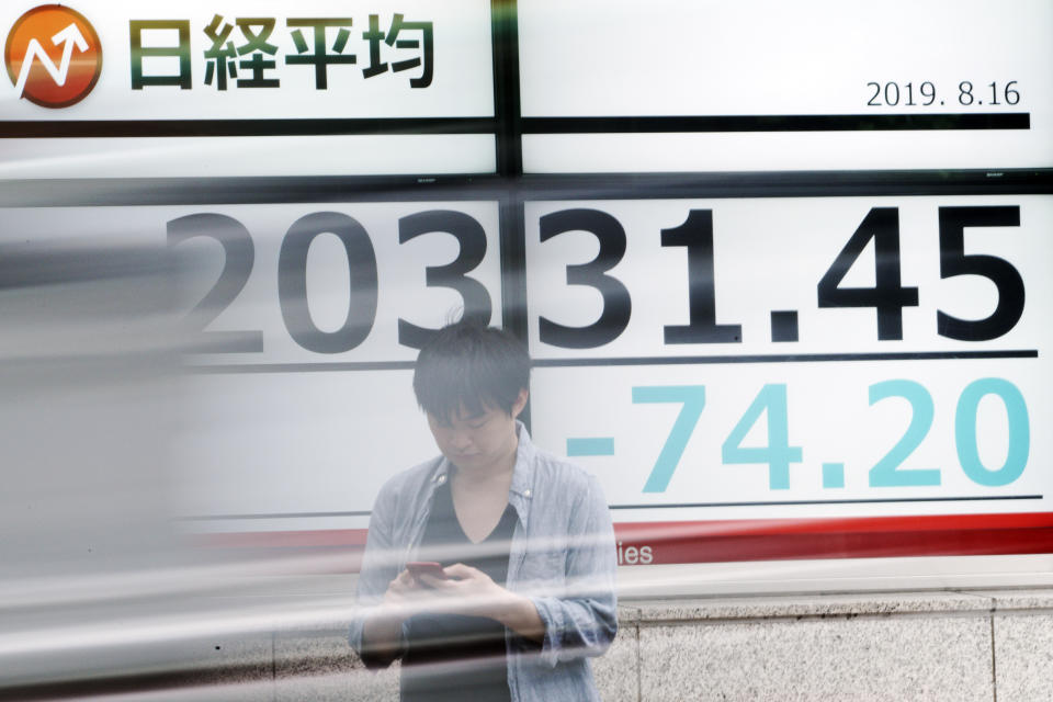 A man stands as a car goes by an electronic stock board showing Japan's Nikkei 225 index at a securities firm in Tokyo Friday, Aug. 16, 2019. Asian shares were mixed Friday as turbulence continued on global markets amid ongoing worries about U.S.-China trade conflict. (AP Photo/Eugene Hoshiko)